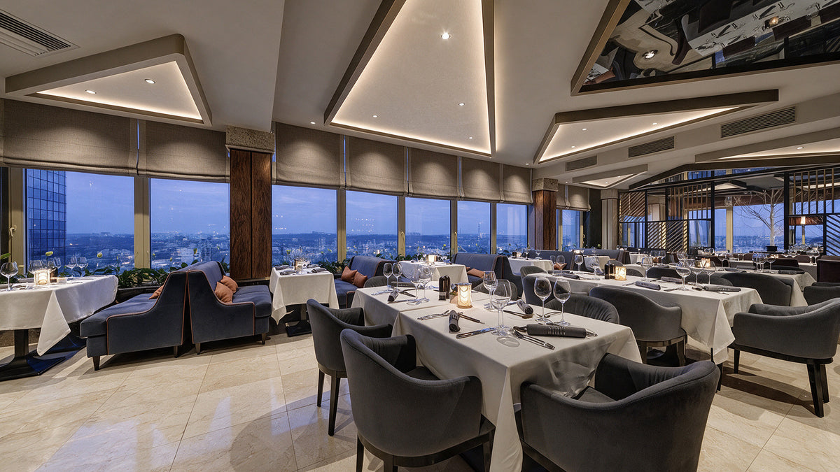 Rooftop restaurant at dusk with grey velvet armchairs and banquettes overlooking Chișinău, Radisson Blu Leogrand