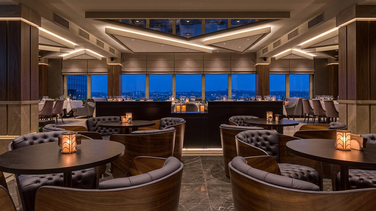 Lounge with button-tufted barrel chairs in walnut shells around round tables, Radisson Blu Leogrand