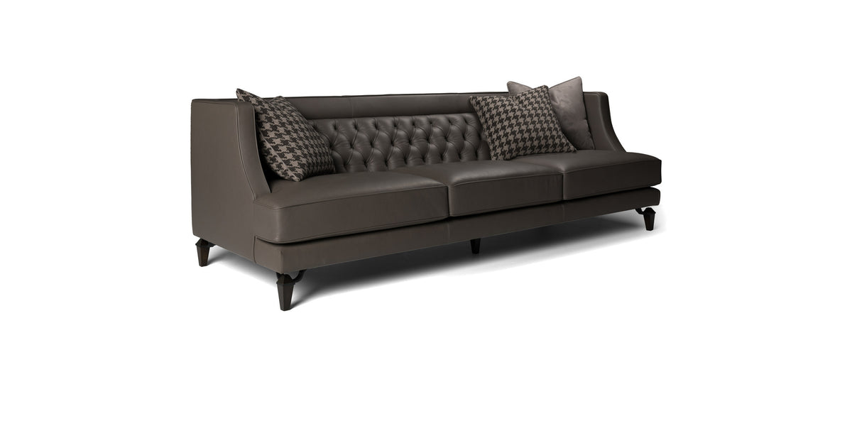Divano Charlotte in pelle grigio scuro con schienale capitonné e cuscini decorativi, vista di tre quarti